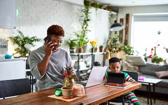 woman talking on her phone and working at the kitchen counter while her son plays on the side